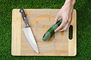 Vegetarians and cooking on the nature of the theme: human hand holding a knife and cucumber on a cutting board and a background of