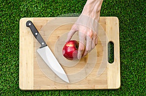 Vegetarians and cooking on the nature of the theme: human hand holding a knife and a red apple on the background of a cutting boar