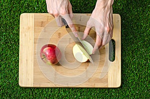 Vegetarians and cooking on the nature of the theme: human hand holding a knife and a red apple on the background of a cutting boar