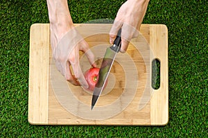 Vegetarians and cooking on the nature of the theme: human hand holding a knife and tomato cutting board on a background of green g photo
