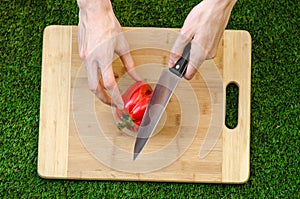 Vegetarians and cooking on the nature of the theme: human hand holding a red pepper and a knife on a cutting board and a backgroun photo