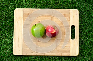 Vegetarians and cooking on the nature of the theme: lying on a cutting board red and green apples on a grass background