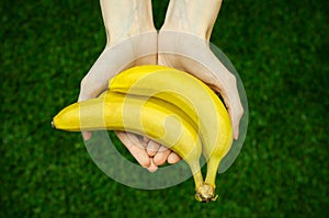 Vegetarians and fresh fruit and vegetables on the nature of the theme: human hand holding a bunch of bananas on a background of gr