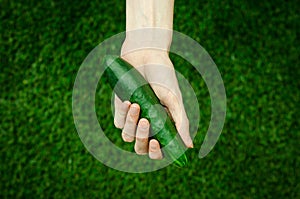 Vegetarians and fresh fruit and vegetables on the nature of the theme: human hand holding a cucumber on a background of green gras