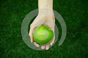 Vegetarians and fresh fruit and vegetables on the nature of the theme: human hand holding a green apple on a background of green g photo