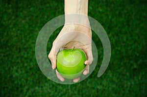 Vegetarians and fresh fruit and vegetables on the nature of the theme: human hand holding a green apple on a background of green g