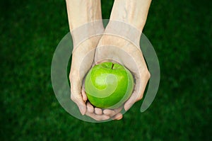 Vegetarians and fresh fruit and vegetables on the nature of the theme: human hand holding a green apple on a background of green g photo