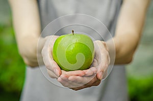Vegetarians and fresh fruit and vegetables on the nature of the theme: human hand holding a green apple on a background of green g