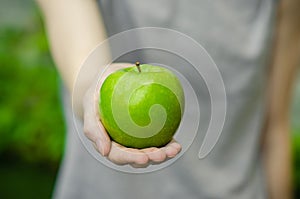 Vegetarians and fresh fruit and vegetables on the nature of the theme: human hand holding a green apple on a background of green g photo