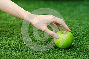 Vegetarians and fresh fruit and vegetables on the nature of the theme: human hand holding a green apple on a background of green g