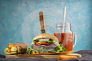 A veggie burger (made from eggplant) in a sesame seed bun with layers of curly lettuce  tomato  cucumber and onion