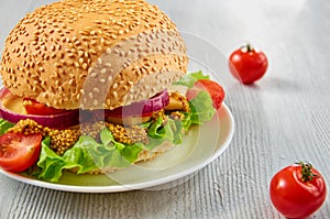 Veggie burger with salad, onion rings decorated with fresh cherry tomatoes on the gray concrete background with free copy space