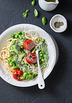 Veggie pasta. Vegetarian lunch - spaghetti with broccoli cabbage, green peas and cherry tomatoes on dark background, top view. Hea