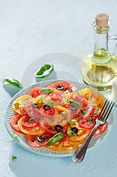 Veggie tomatoes summer salad with basil and olives on blue table.