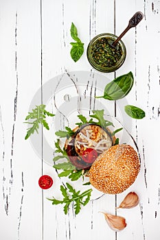 Veggies burger served on cutting board over white rustic table. Vegan grilled eggplant, arugula, sprouts and pesto sauce burger.