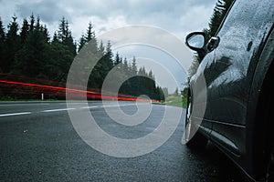 Vehicle lights trails and wet car on roadside