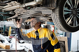 Vehicle mechanic conduct car inspection from beneath lifted vehicle. Oxus