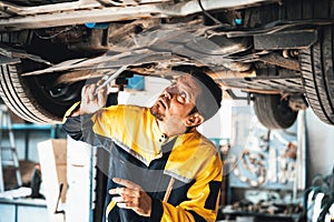 Vehicle mechanic conduct car inspection from beneath lifted vehicle. Oxus