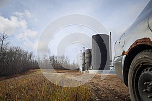 Vehicle parked in front of bitumen oil storage tanks on an oil lease