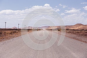 Vehicle seen from afar travelling on dusty dirt road in desert area during a sunny hazy morning