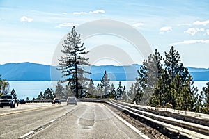 Vehicles rounding a bend with a battered guard rail near Lake Tahloe CA USA with lake and mountains in distance