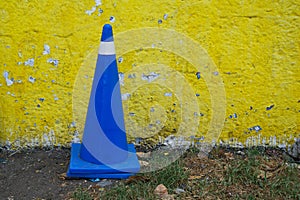 Vehicular control cone in royal blue color against a yellow wall