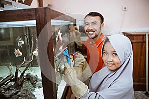 veiled daughter smiling while cleaning aquarium glass with dad