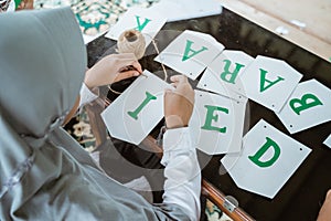 veiled girl making flag chain paper decoration for Eid Mubarak
