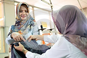 veiled Muslim supervisor with a hand gesture pointed at the cloth held by the tailor