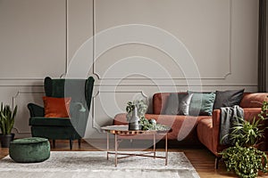 Velvet emerald green armchair with orange pillow next to corner sofa and coffee table