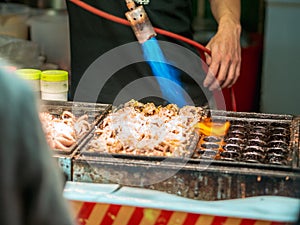 Vendor making giant Takoyaki with cheese using blowtorch to speed up the cooking.