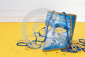 Venetian carnival blue mask with beads on a yellow background.