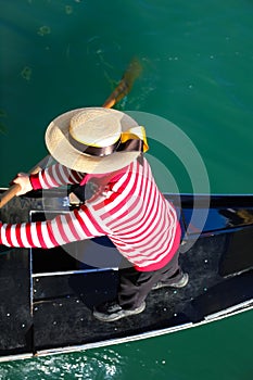 Venetian gondolier with hat rowing on gondola boat on the water of grand canal in Venice Italy