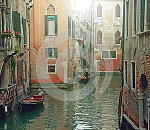 Venetian gondolier punting gondola through green canal waters of Venice Italy.