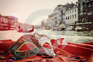 venetian mask on red silk fabric in front of blurry Venice