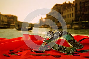 Venetian mask on red silk fabric in front of blurry Venice