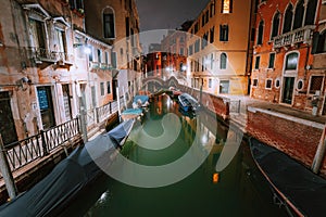 Venezia Italy. Narrow channel and gondola boats in lagoon city venice at night. Vivid colored old brick buildings around