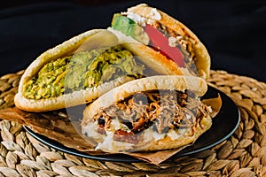 Venezuelan arepas on a black background, made with maize and filled with avocado, tomato, meat, cheese and black beans photo