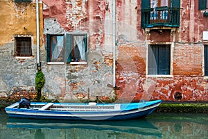 Venice cityscape, boat on narrow water canal near colorful wall with windows