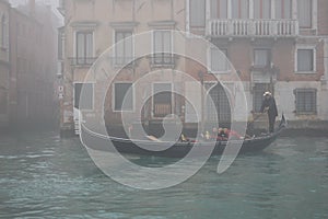 Venice in the fog. Gondolier carries tourists on the canal in the gondola.