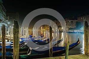 Venice Italy Grand Canal night view of traditional buildings and moored empty gondolas rocking next to wooden wharf pilings