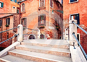 Venice, Italy. Small bridge with concrete steps and traditional orange historic buildings.
