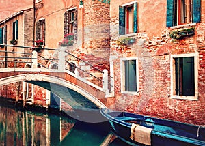 Venice, Italy. Small bridge over canal with blue boat and traditional orange historic buildings.