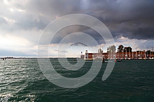 Venice, the lighthouse Faro of San Giorgio Maggiore island viewed from water, from sailboat with dark blue stormy sky at