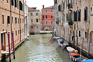 Venice water canal, typical Venetian architecture, boats parked by the canal, blue and red posts on the Venice canal, greenish wat