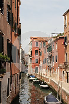 Venice water canal, typical Venetian architecture, boats parked by the canal, blue and red posts on the Venice canal, greenish wat