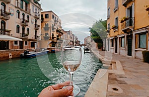 Venice with water canals and white wine glass in hand of happy traveler, Italy. Ancient italian city