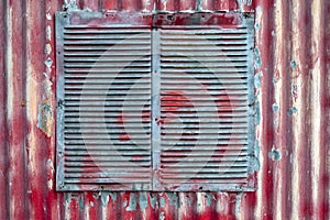 A vent in the wall of a red corrugated metal building