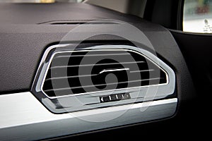 Ventilation exhaust in black car interior with metal frame.