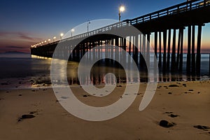 Ventura Pier at Sunset. Beach in foreground, smooth ocean; colored sky in background.